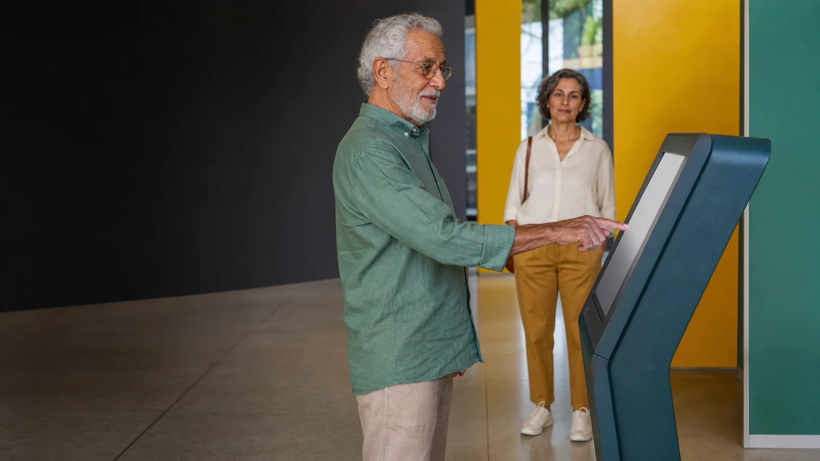 Homem idoso testa um terminal de autoatendimento em um centro cultural colorido.